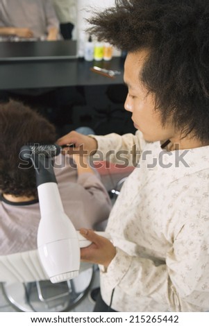 Hairdresser blow-drying man\'s hair with hair dryer in salon, close-up, rear view