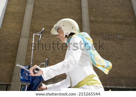 Woman in crash helmet riding on scooter in street, smiling, profile, low angle view