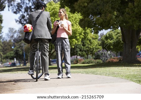 Man sitting on bicycle with bunch of flowers in bag, flirting with woman on path in park