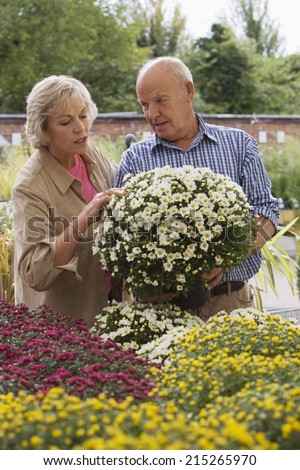 Senior couple shopping for flowers in garden centre, man holding pot plant
