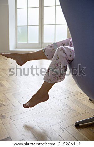 Woman in pyjamas sitting in armchair at home, feet up, side view, low section