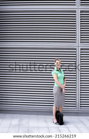 Businesswoman in green short-sleeved blouse and grey skirt standing on pavement, portrait