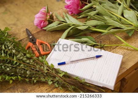 Pink flowers on table beside order pad and scissors in flower shop, close-up (still life)