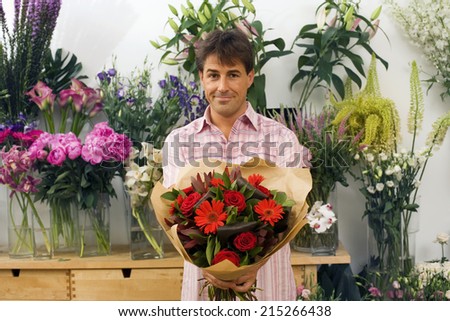 Man holding bouquet of flowers beside display in flower shop, smiling, front view, portrait