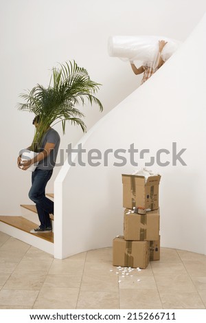 Couple moving house, man carrying large pot plant down staircase, woman carrying dust sheet, profile