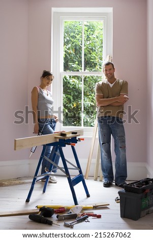 Couple doing DIY at home, woman holding glue gun beside timber on workbench, smiling, portrait