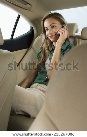 Businesswoman sitting in back seat of car, using mobile phone, smiling