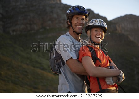 Couple in cycling helmets standing in mountain valley, smiling, side view, portrait