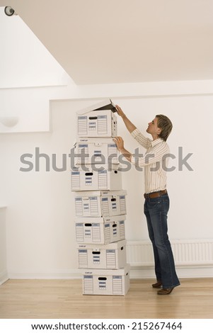 Businessman standing beside tall stack of file boxes in empty office, opening lid of top box