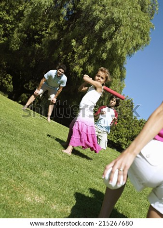 Two generation family playing softball in park, girl (6-8) batting, smiling (tilt)