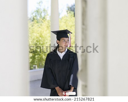University student in graduation gown and mortar board holding diploma, smiling