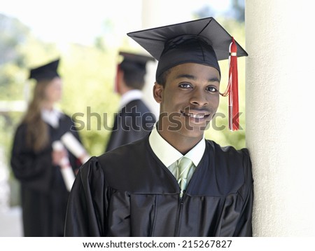 University student in graduation gown and mortar board, smiling, portrait, focus on foreground