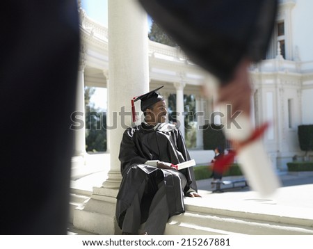 University student in graduation gown and mortar board holding diploma, smiling, focus on background