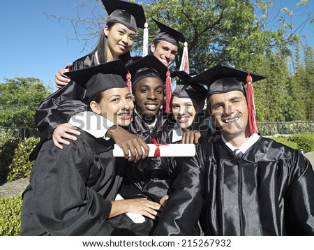 University students in graduation gowns and mortar boards holding diplomas, smiling, portrait