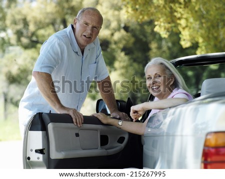 Senior couple posing beside convertible car, woman sitting in driver\'s seat, smiling, portrait