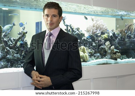 Businessman standing beside fish tank, smiling, portrait