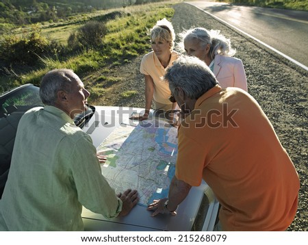 Two senior couples standing beside convertible car, looking at road map, elevated view