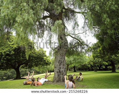 Group of children playing ring-a-ring-o'roses in park, falling down beside tree
