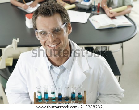 Science teacher standing in classroom, holding rack of test tubes, smiling, portrait, elevated view