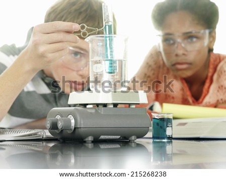 Teenage boy and girl (15-17) doing science experiment at desk in classroom, surface level