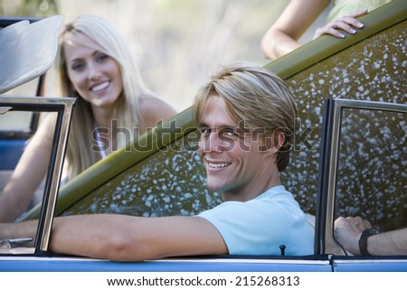 Teenage couple sitting in car with surfboard, smiling, side view, portrait