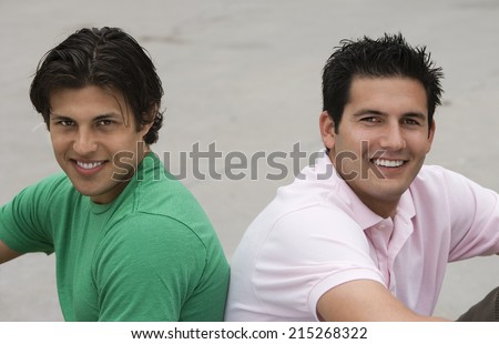 Two men sitting back to back on ground, smiling, side view, portrait