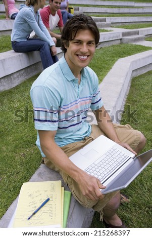 Teenage boy studying outdoors with friends, using laptop, smiling, portrait