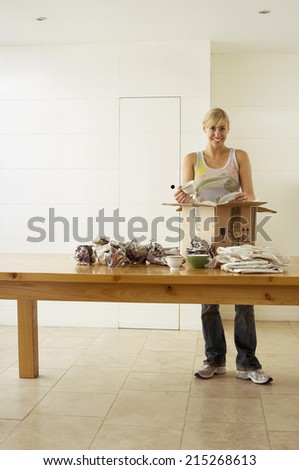 Woman moving house, packing crockery wrapped in paper in box on dining room table, smiling, portrait