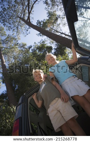 Boy and girl standing in car boot, smiling, portrait, low angle view (tilt)