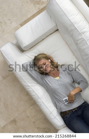 Woman relaxing on sofa at home, listening to MP3 player, smiling, portrait, overhead view