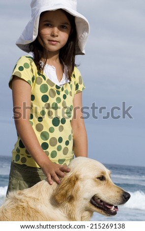 Girl (6-8) in sun hat standing on beach with dog, smiling, side view, portrait