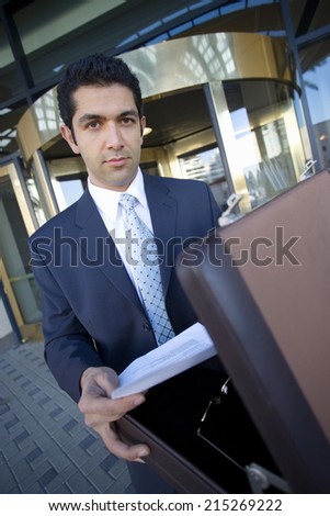 Businessman standing in front of revolving door, taking document from briefcase, portrait (tilt)