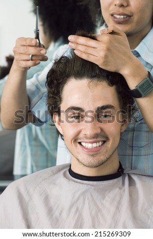 Hairdresser cutting man\'s hair in barbers shop, smiling, front view, close-up, portrait
