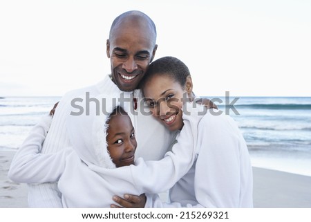 Two generation family in white clothing embracing on beach, smiling, close-up, portrait