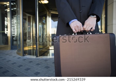 Businessman standing in front of revolving door, holding briefcase, mid-section