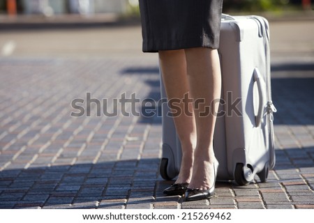 Businesswoman in skirt and high heels standing with luggage, low section
