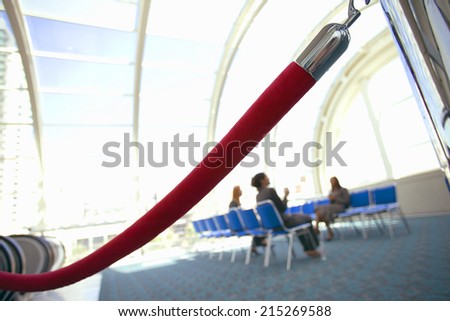 Business people sitting in airport departure lounge, focus on rope barrier in foreground (tilt)