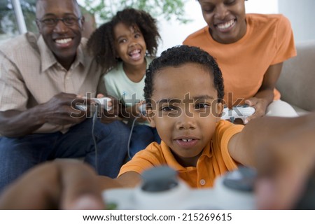 Family playing video games console on sofa at home, smiling, front view (differential focus)