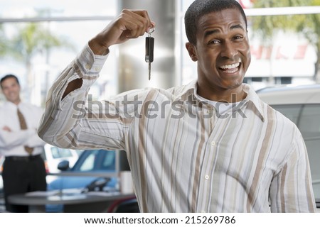 Salesman in car showroom, focus on male customer holding key in foreground, smiling, portrait