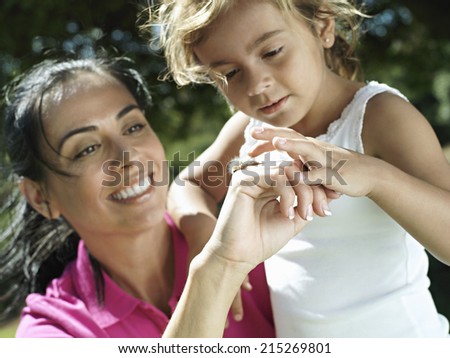 Mother and daughter (6-8) looking at bug on hand, smiling, close-up (tilt)