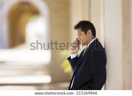 Businessman leaning against wall in building arcade, using mobile phone, profile