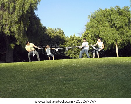 Two generation family playing tug-of-war on grass in park, side view
