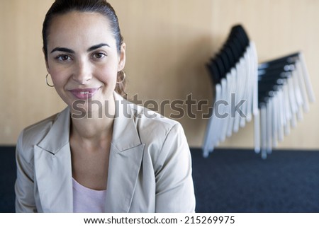 Stack of chairs in conference room, focus on businesswoman in foreground, smiling, portrait