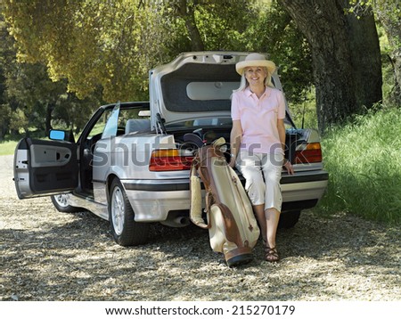 Senior woman leaning on car boot beside golf bag, smiling, portrait