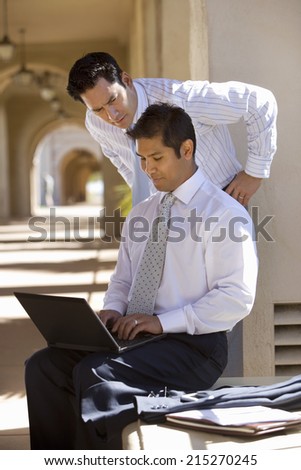 Two businessmen working in building arcade, man using laptop, side view