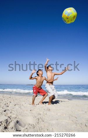Two boys (6-8) playing with inflatable ball on sandy beach, Atlantic Ocean in background, smiling, side view