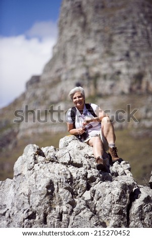 Mature woman hiking on mountain trail, sitting on rock, taking break, smiling, portrait
