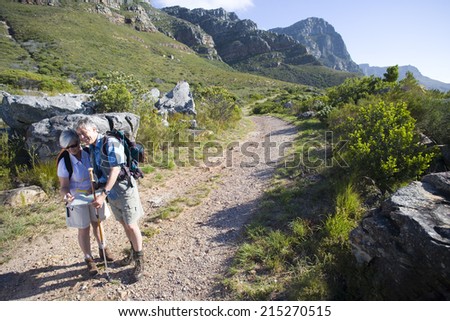 Mature couple, with rucksacks, hiking on mountain trail, looking at map, man leaning on hiking pole