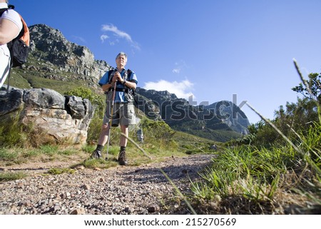 Mature man, with rucksack and hiking pole, standing on mountain trail (surface level)