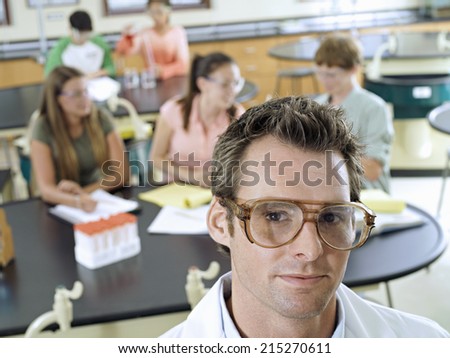 Teenagers (15-17) sitting at desks in classroom, focus on science teacher in foreground, portrait